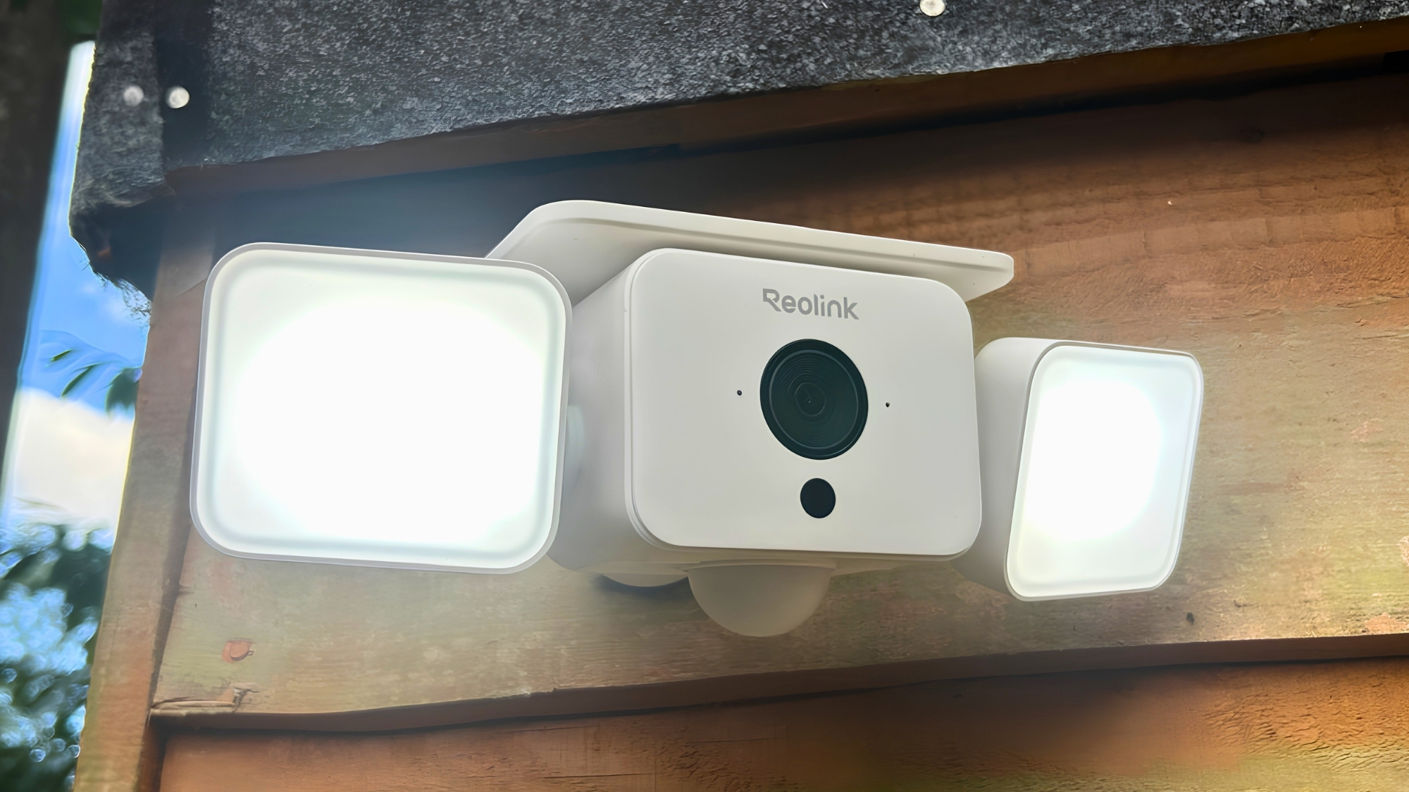 Reolink floodlight camera mounted under eaves, two bright lights either side of central lens, close-up.