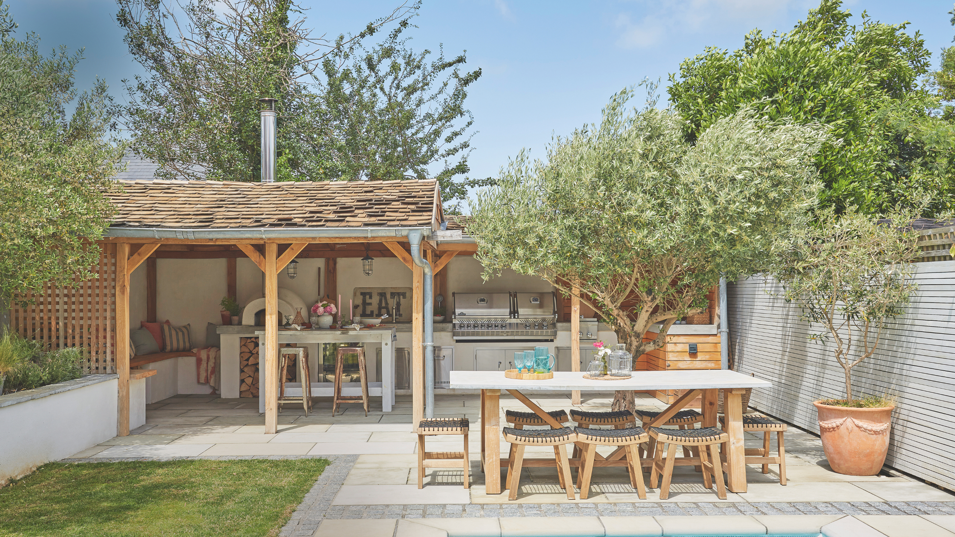 Garden kitchen built under a pergola. There is a garden dinng table next to it.