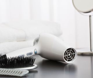A white hairdryer laying on a table beside a black brush