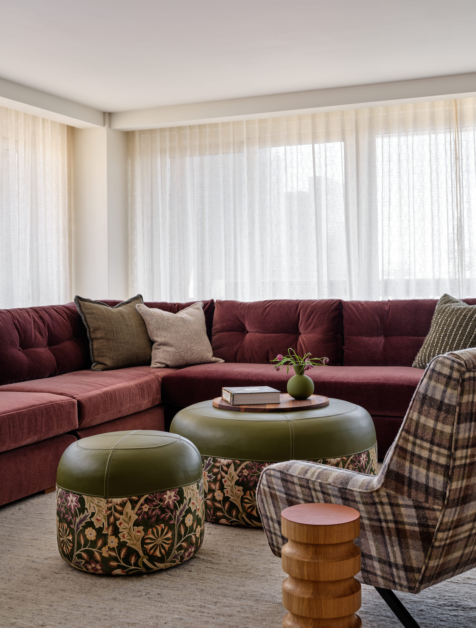 neutral living room with burgundy sofa, green patterned ottoman, tartan armchair, and timber side table