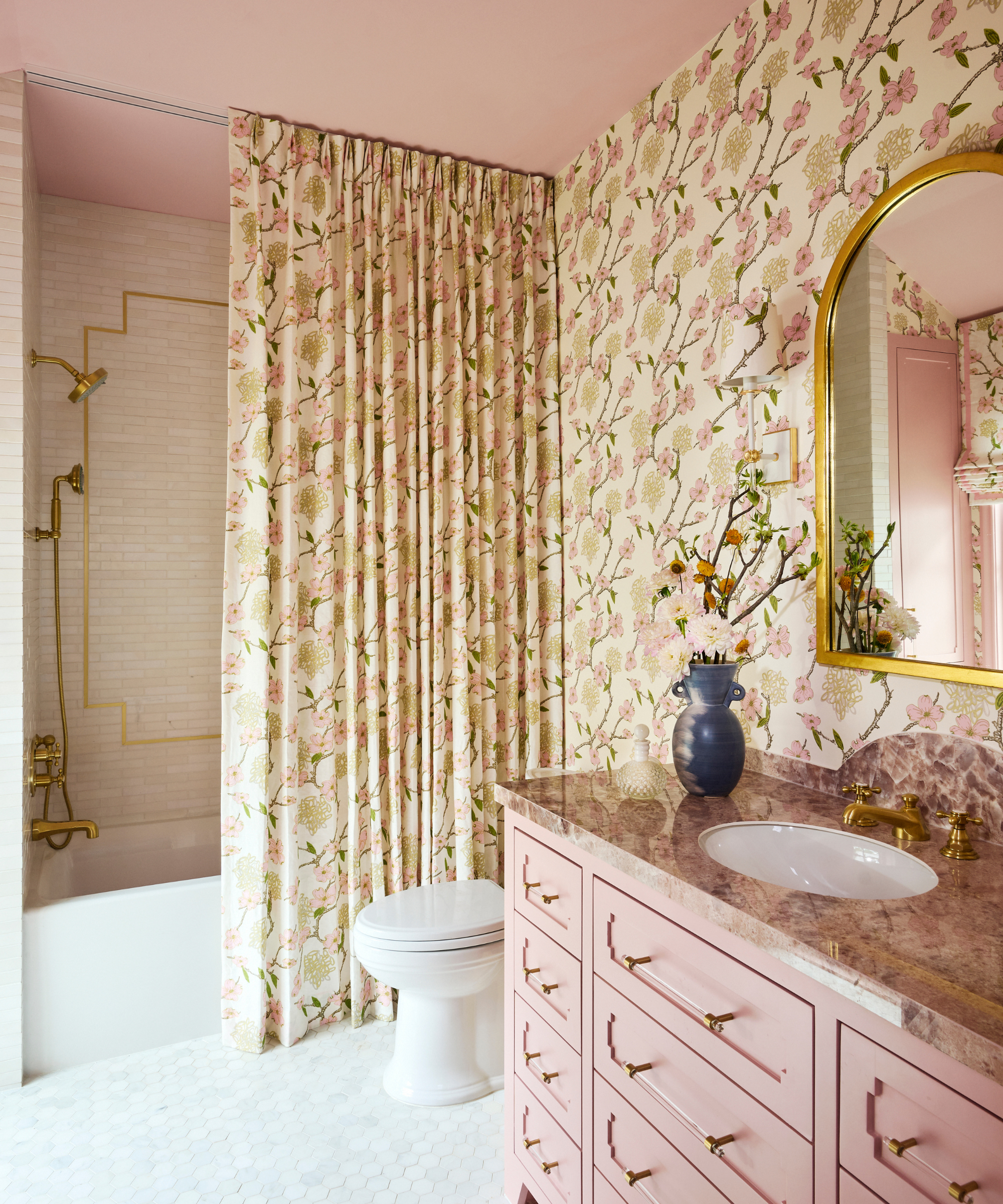 a bathroom with a pink vanity and a pink ceiling, floral wallpaper that matches the tall shower curtain, and a white tile floor