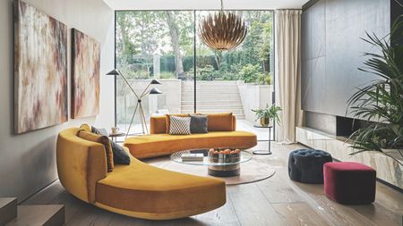 Living room with orange semi circular sofa on wooden floor, glass walls out to patio and garden.