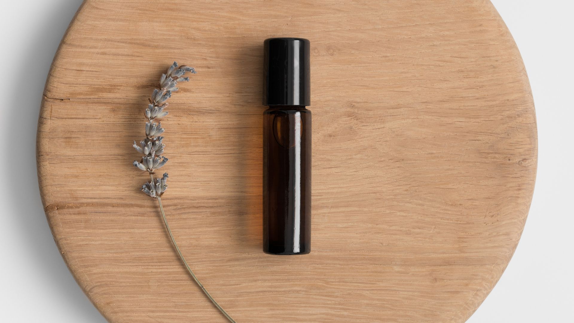 Lavender oil roll-on on a wooden block neck to a single stem of lavender.