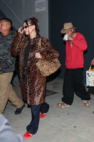 Hailey Bieber wearing a leopard print coat and bag with black pants and red sneakers.