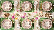 Tablescape shot from above with a pink and green theme, layered plates, mats and gold cutlery and flowers in the center