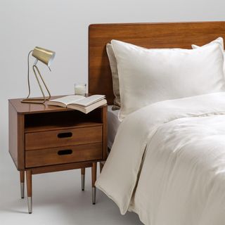 White bedding next to wooden headboard and bedside table