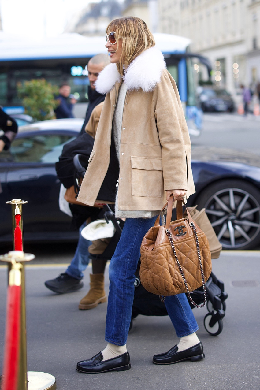 Bella Hadid wearing a tan coat, cream sweater, cropped flare jeans, socks, and loafers in Paris during PFW F/W 26.