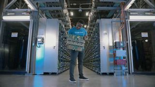 A photo of a person holding a Google Cloud TPU server board, against a background of many TPU servers