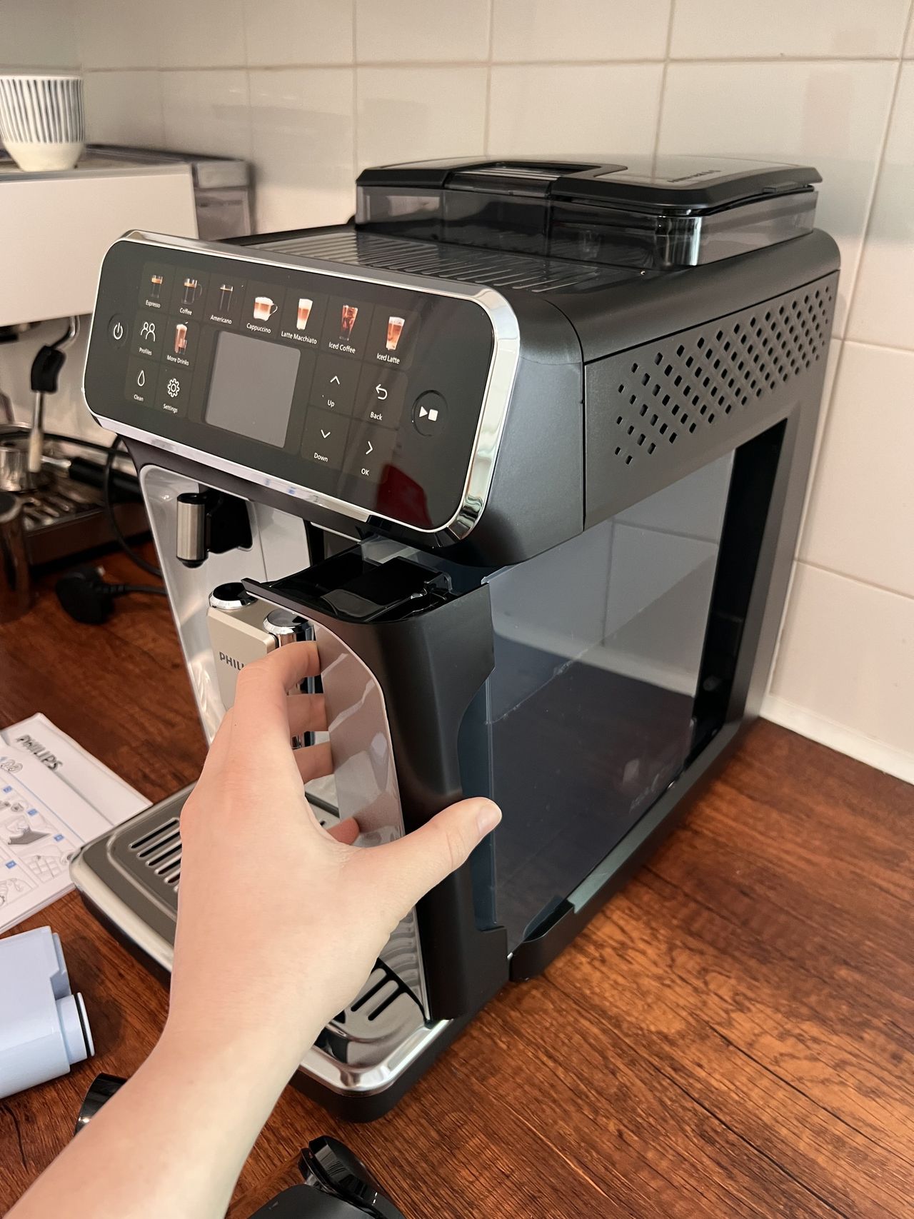 Hand putting the water tank into the Philips 5500 Series on a wooden kitchen countertop.