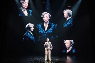 sarah snook starring in the picture of dorian gray on broadway wearing a tan suit while images of her in a blue suit is projected on screens around her