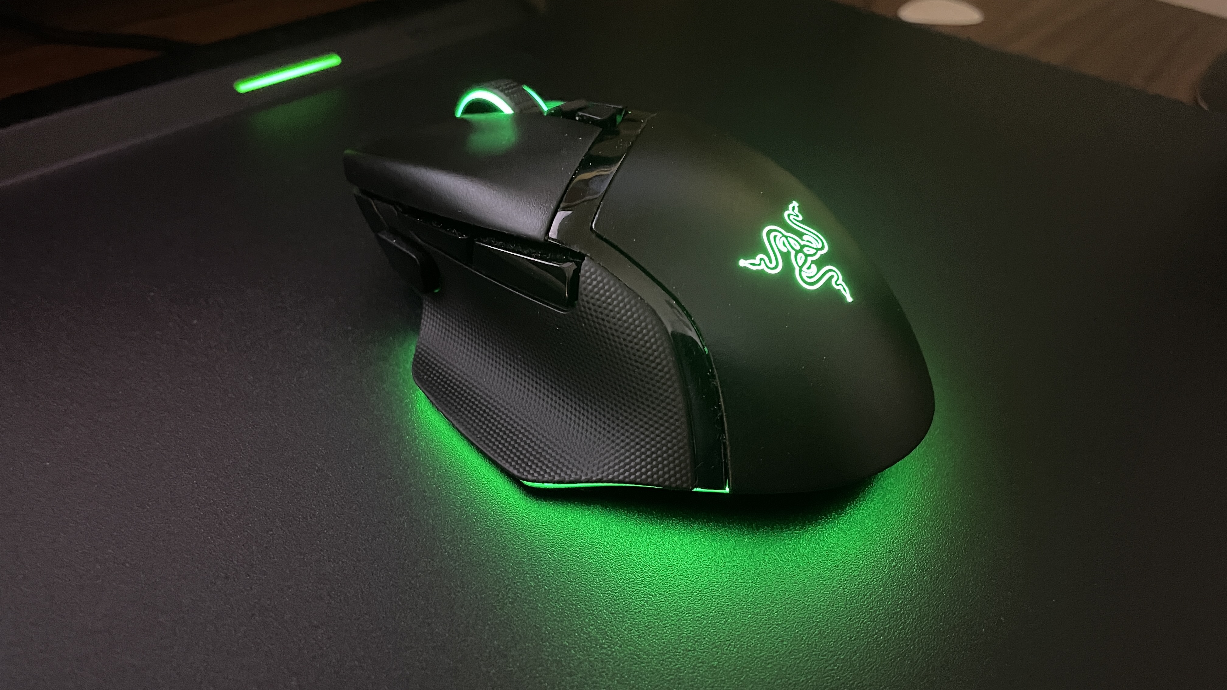 A Razer Basilisk V3 Pro with green RGB underglow lighting on top of a mouse pad on a desk