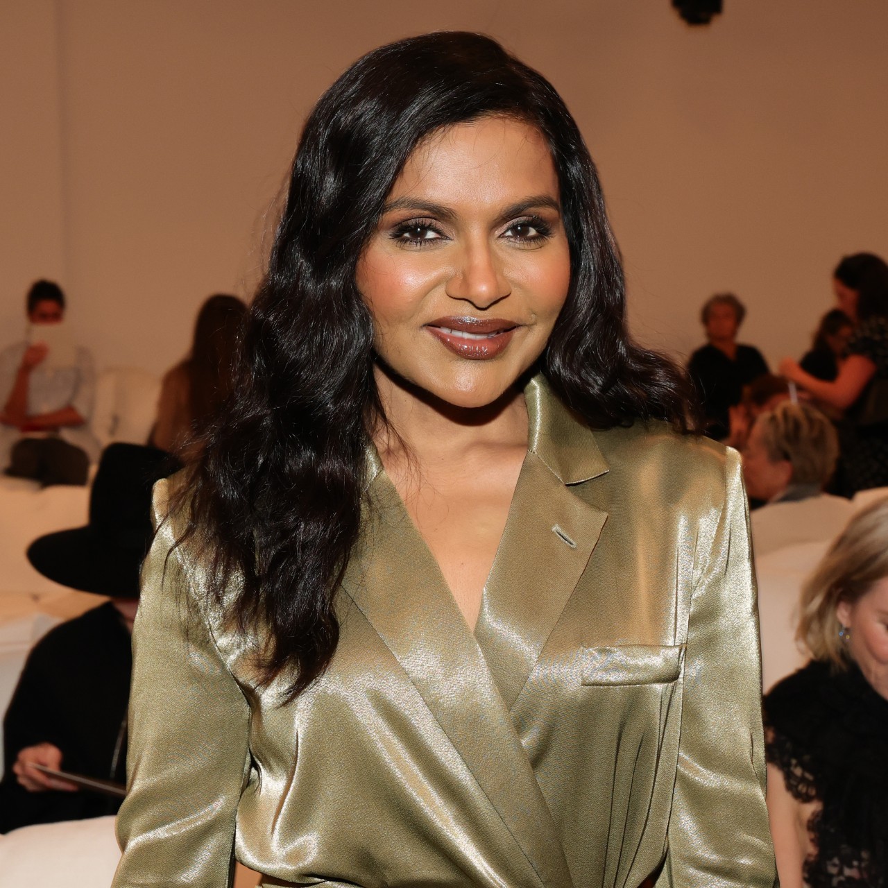 a woman with dark hair wearing a gold blazer dress