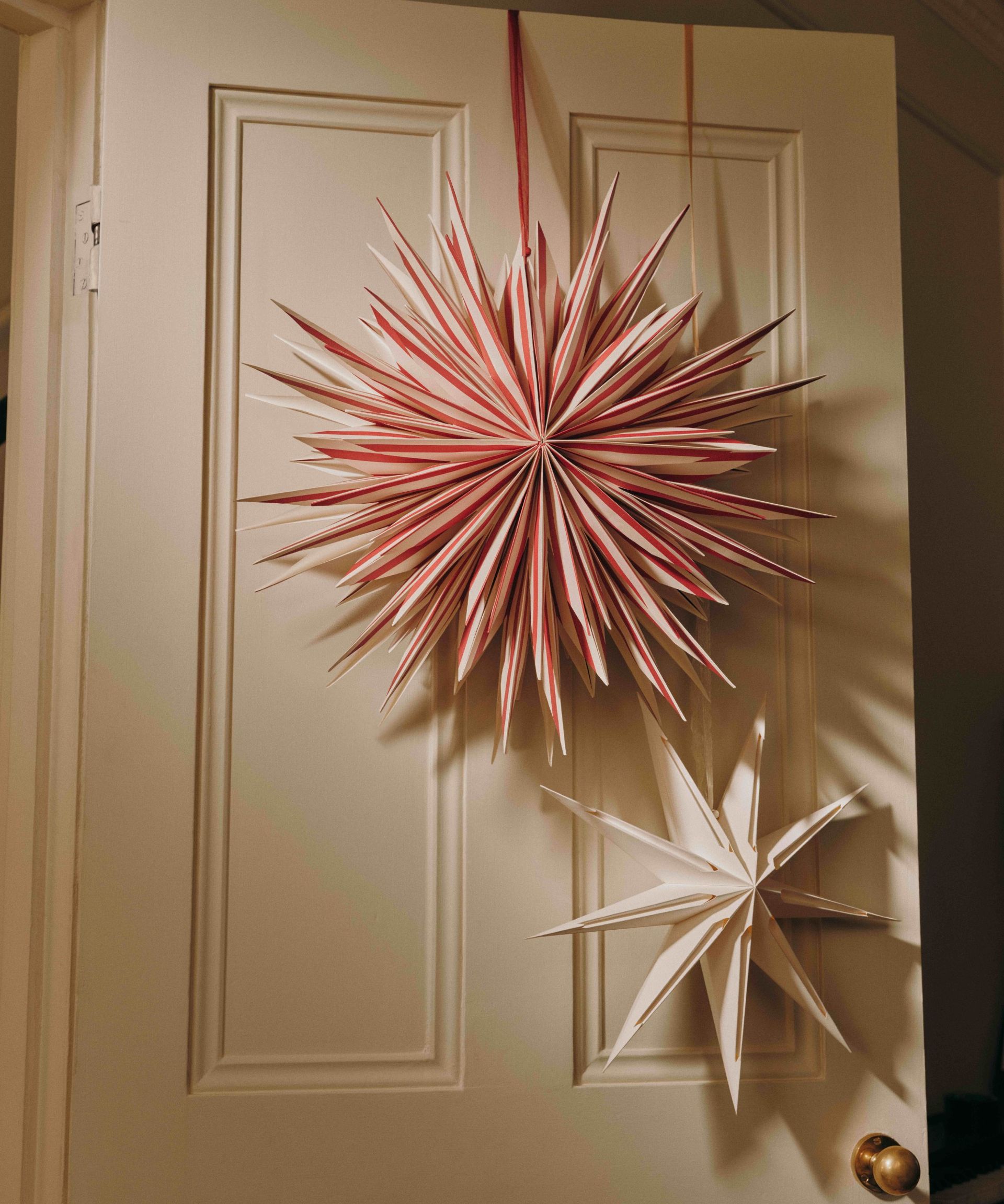 An off-white door decorated with a large red striped Christmas paper star from M&S and a smaller white star with cut-outs, also from M&S