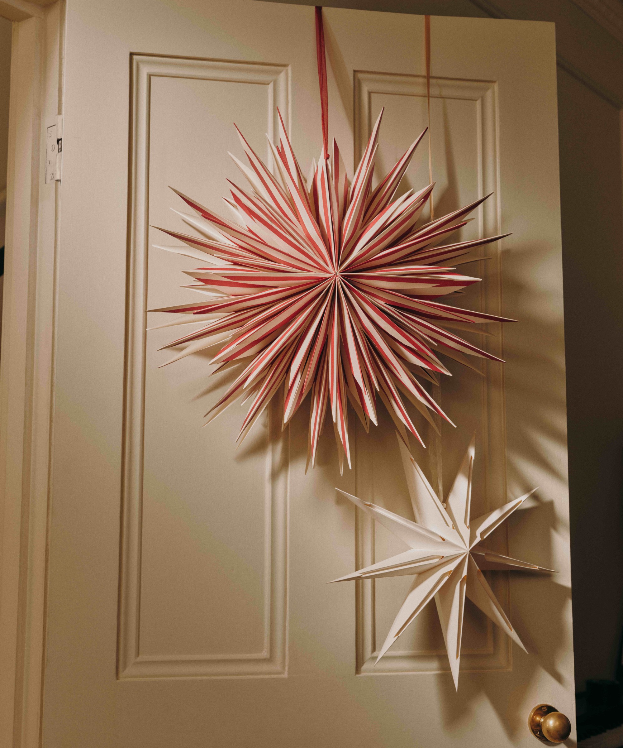 An off-white door decorated with a large red striped Christmas paper star from M&amp;amp;S and a smaller white star with cut-outs, also from M&amp;amp;S