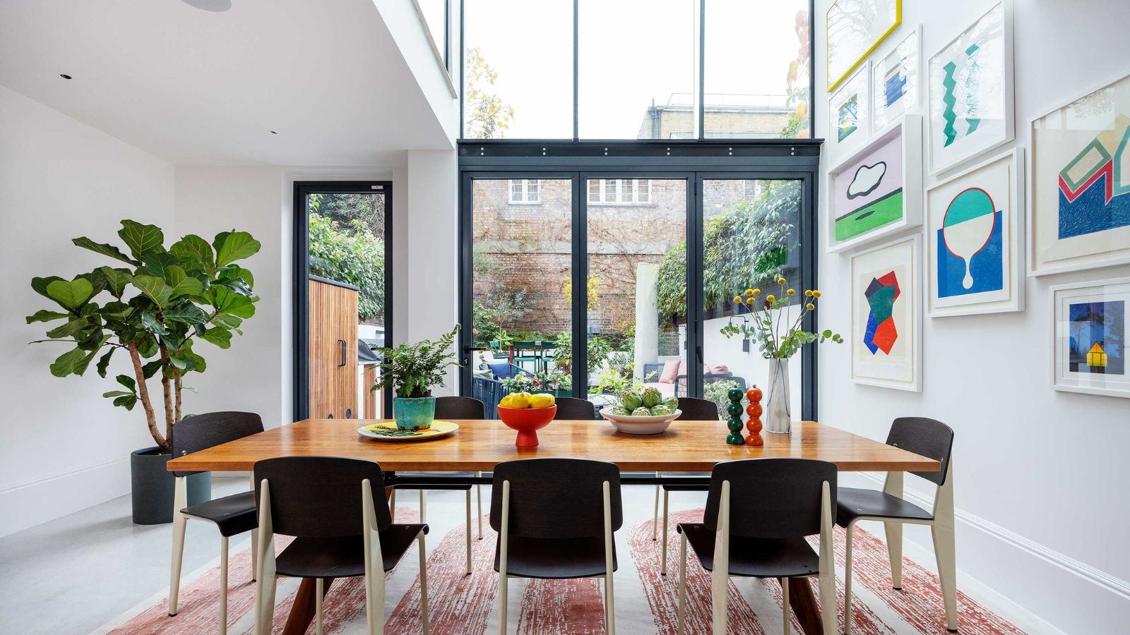 White sunroom with high ceilings and floor to ceiling windows. Dining table for eight with colorful wall art, rug and potted plant
