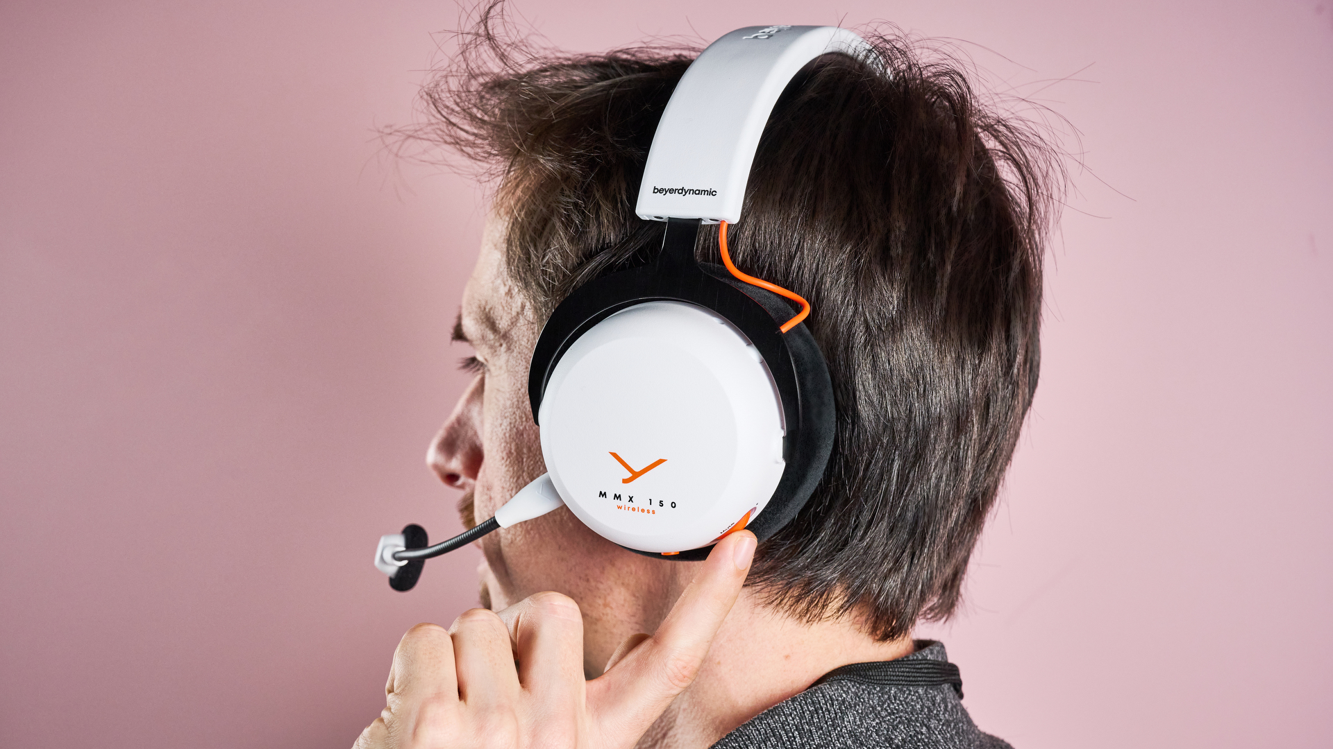 The Beyerdynamic MMX 150 Wireless on a man&#039;s head from a rear angle; he is spinning the volume wheel on one earcup with one finger.