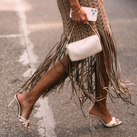 Woman crossing the street wearing fringe dress and white bag with white heels 