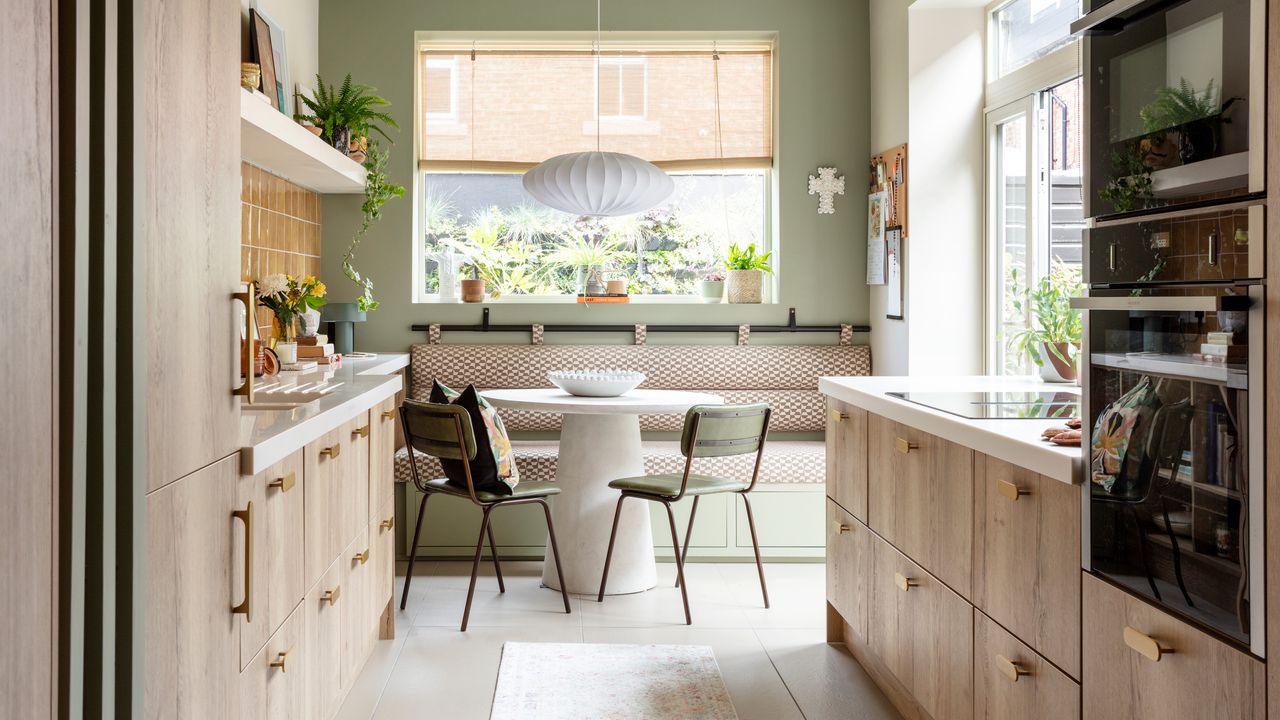 a pale green and beige kitchen with wooden cabinetry and banquette seating around a round dining table