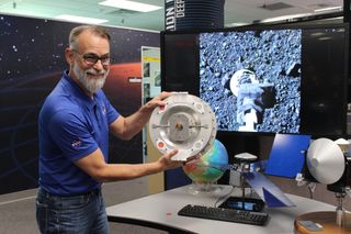 a scientist in a blue shirt and glasses holding a metal disk