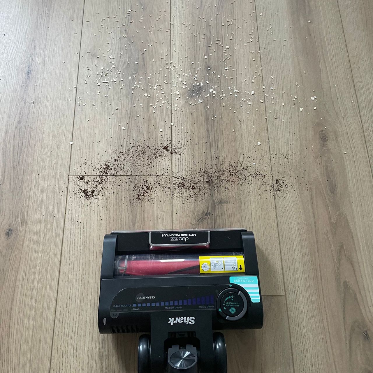 Vacuum on wood-effect laminate floor about to pick up coffee grounds and oats