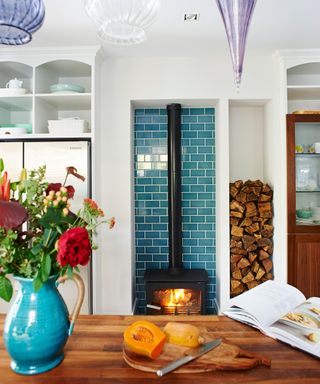 Kitchen color ideas with colorful tiled fireplace and jug on table in foreground.