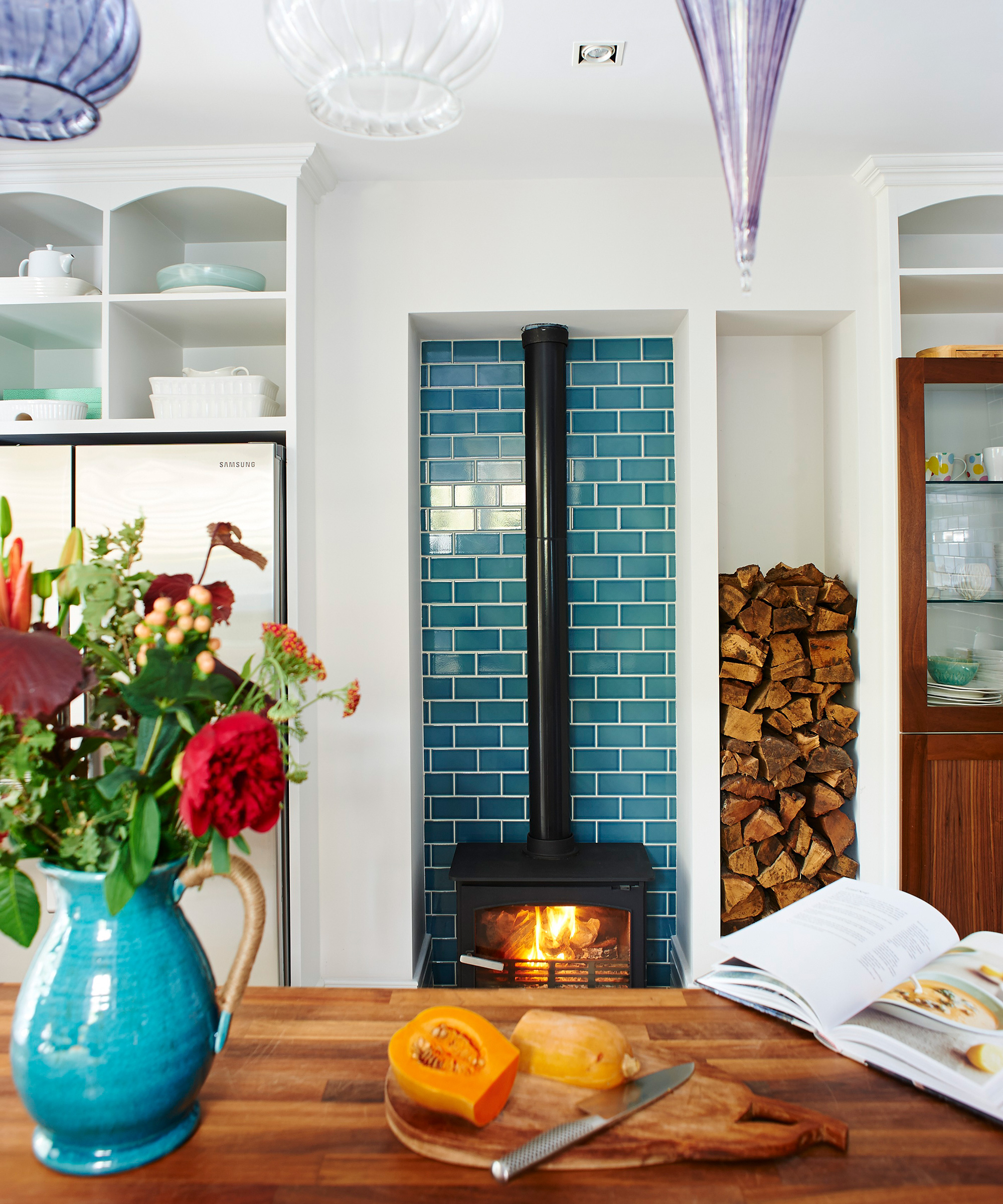 Kitchen color ideas with colorful tiled fireplace and jug on table in foreground.