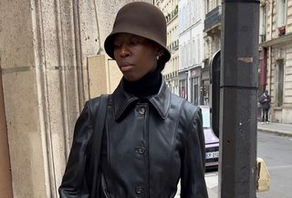 Woman wearing black leather coat with brown hat on the streets of Paris.