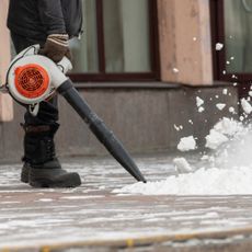 Man uses leaf blower to clear snow from sidewalk