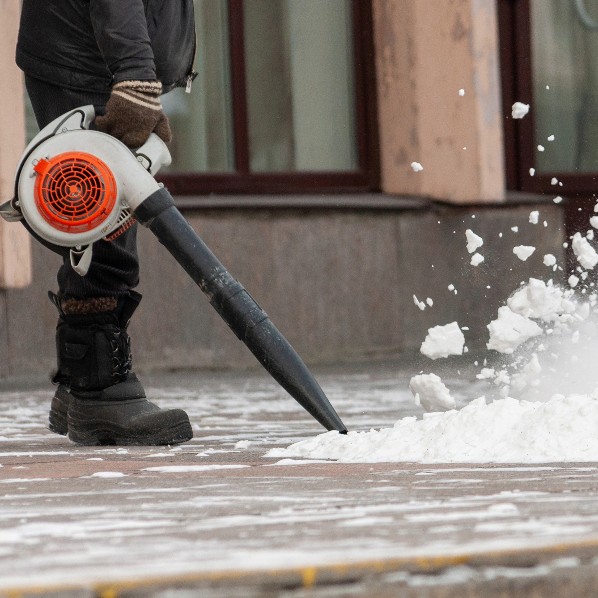Man uses leaf blower to clear snow from sidewalk