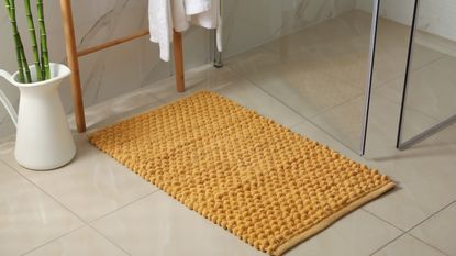 Yellow bath mat on floor in front of shower door with bamboo plant