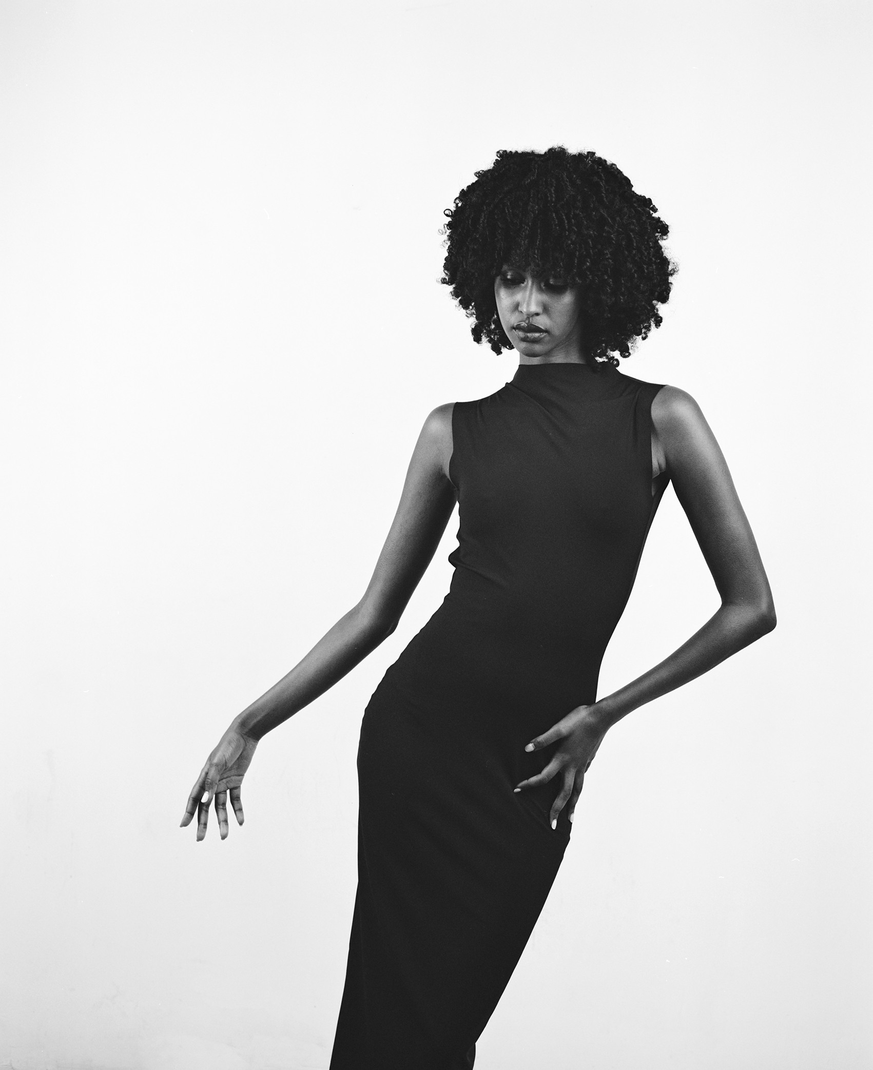 Elegant black and white portrait of a woman in a form-fitting dress, posing gracefully against a plain backdrop