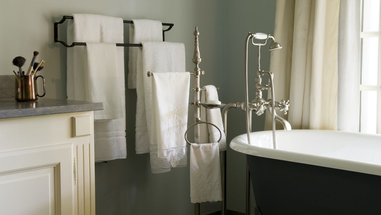 A small green vintage bathroom with a black towel rack on the wall next to the freestanding bathtub