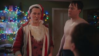 Half naked Sgt Healy looks suspiciously at Billy who is grinning in a Santa hat.