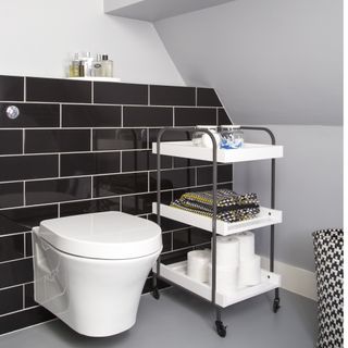 White bathroom, black tiles, toilet, mobile storage trolley, gabled roof