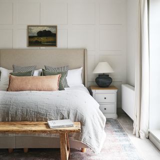 a neutral coloured bedroom with square wall panelling linen bedlinen and rustic bench