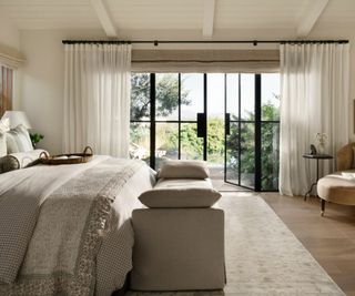 neutral farmhouse bedroom designed by shea mcgee with large double doors leading out to the garden