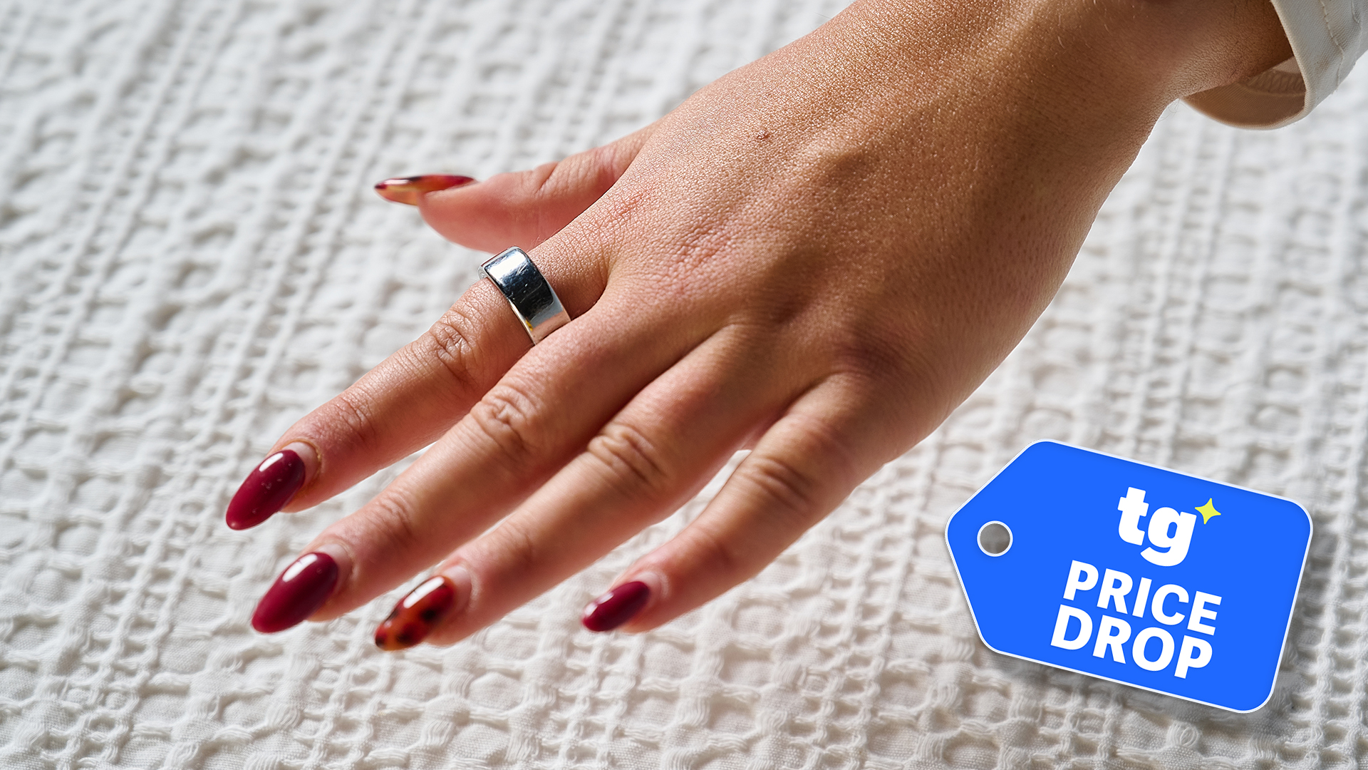 A close up of a hand wearing the Oura Ring 4 in silver. IN the bottom right corner is a Tom's Guide Price Drop deals graphic