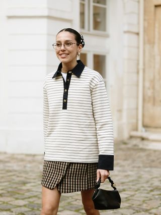 women in a white striped shirt, plaid skirt, and black bag