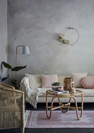 living room with grey textured walls, a cream sofa, pick cushions and a bamboo boho coffee table