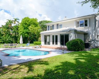 Backyard view of a modern two-story single family detached home with yard and swimming pool in Miami, Florida