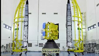 A golden satellite posed between the clamshell-like rocket fairing for India's INSAT-3DS mission.