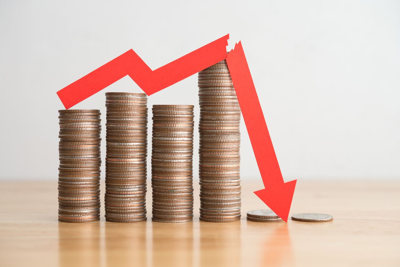 Stack coins and red arrow graph chart falling down on wooden table background.