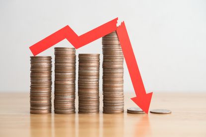 Stack coins and red arrow graph chart falling down on wooden table background.