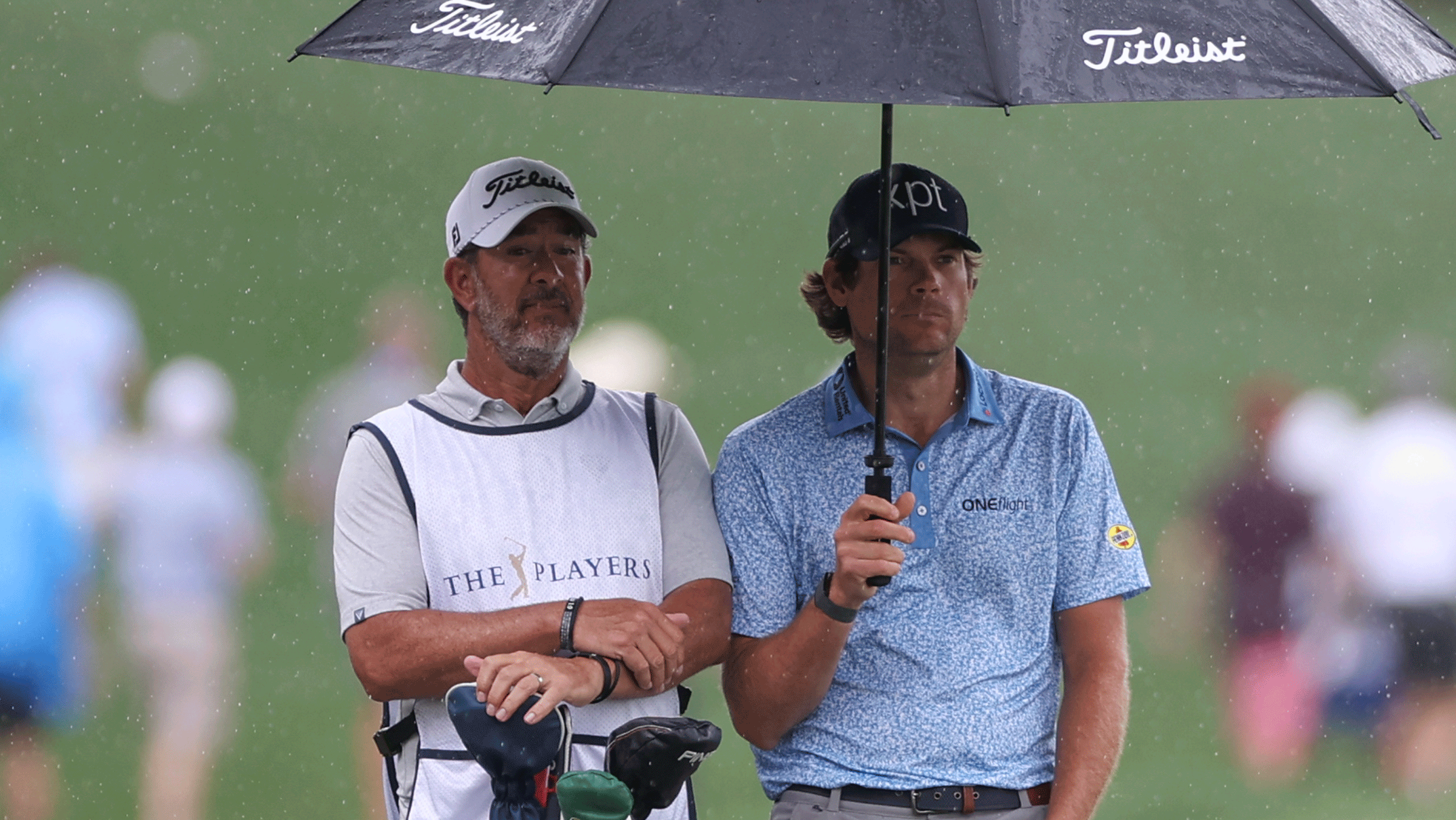 Paul Tesori and Adam Schenk stand under an umbrella during The Players Championship in 2026