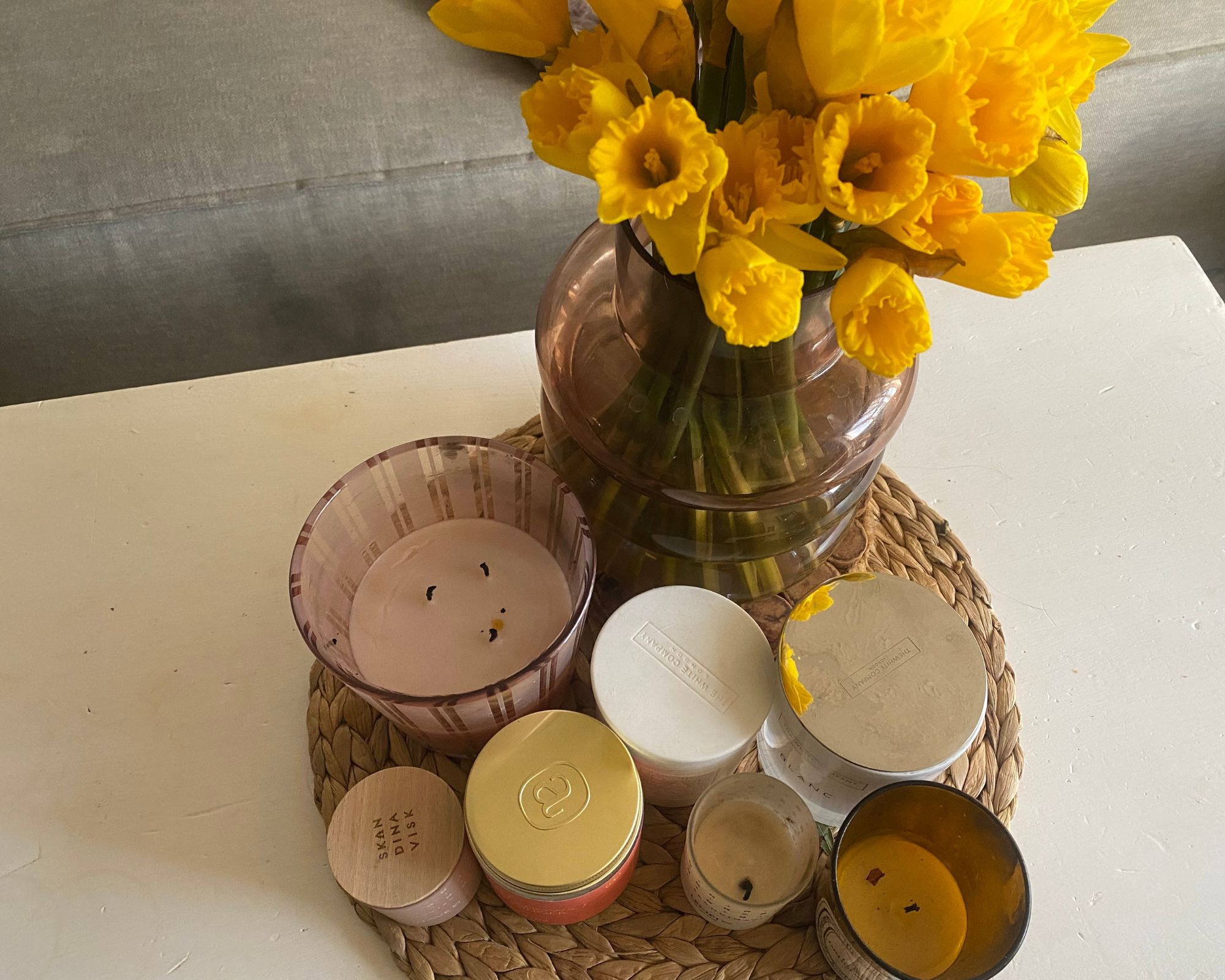 A range of scented candles on Annie's white coffee table with a bunch of daffodils in shot