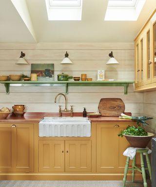 cozy kitchen with yellow cabinets, wood clad white walls, green shelf, butler's sink