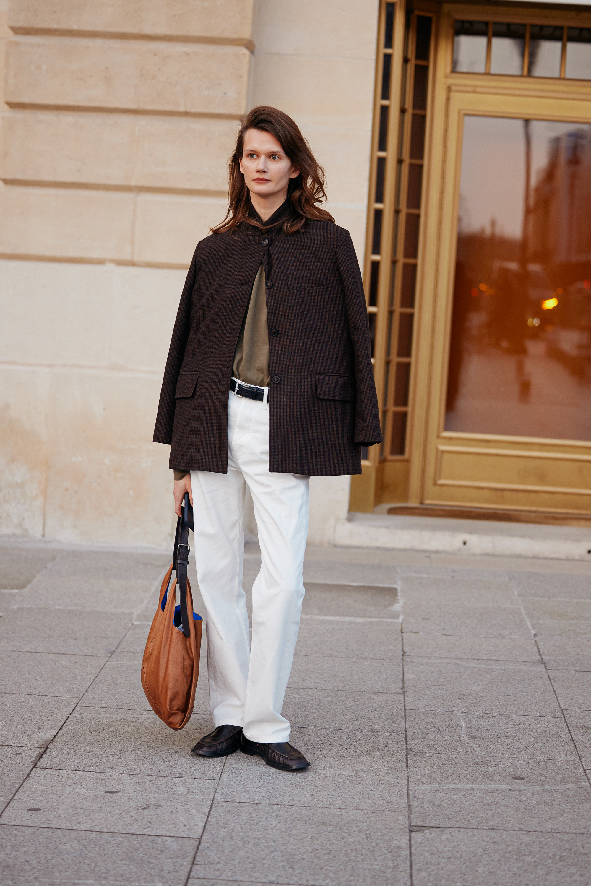 Woman in white jeans, a brown blazer loafers, and a leather tote.