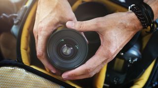 Hands holding a lens above a camera bag