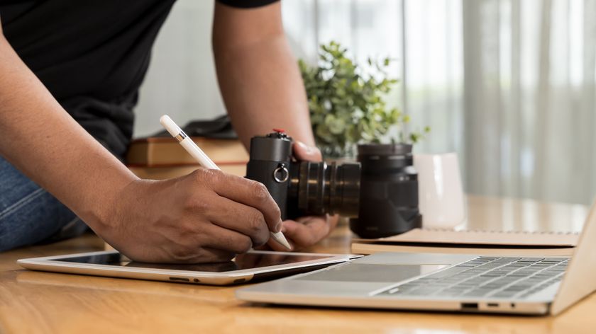 A person writes on a graphic tablet with a camera in his hand and a laptop on the table
