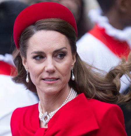 Kate Middleton wearing a red headband and coat with her hair blowing in the breeze on Commonwealth Day 2025